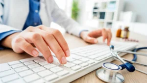 Clinician entering an ICD-10 diagnosis code at a keyboard with a stethoscope on the desk