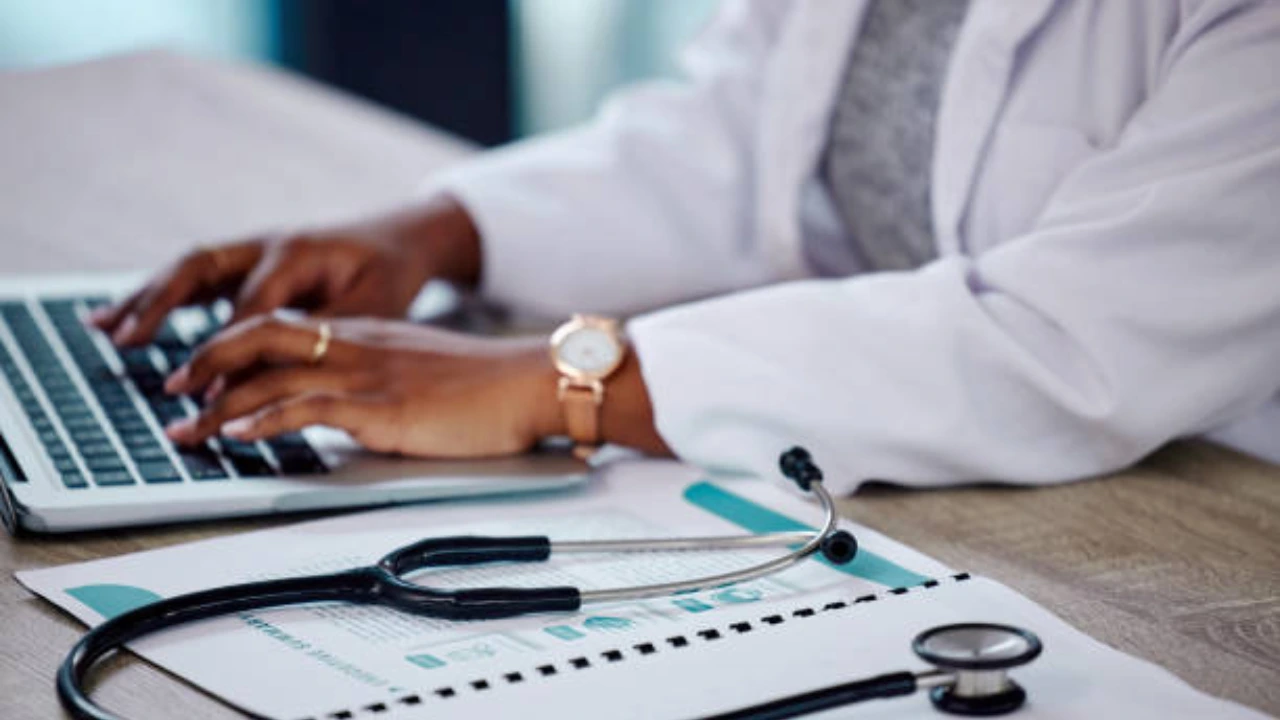 Clinician typing on a laptop beside a stethoscope and benefits report, representing mental health parity enforcement and claim denials